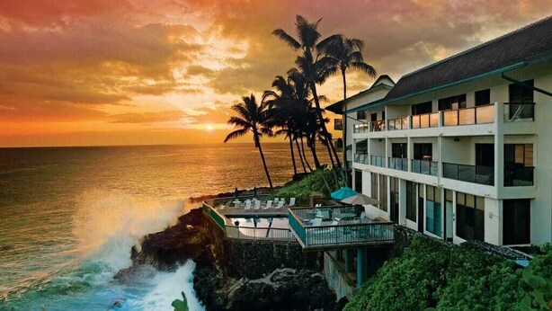 Un hôtel doté d’une piscine donnant sur l’océan, bordé de palmiers, et offrant une vue imprenable sur le coucher du soleil.