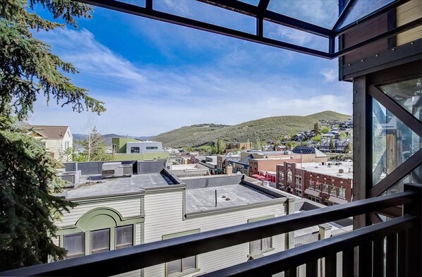 A view from a balcony with a clear sky, overlooking a town with buildings and a hill in the distance.
