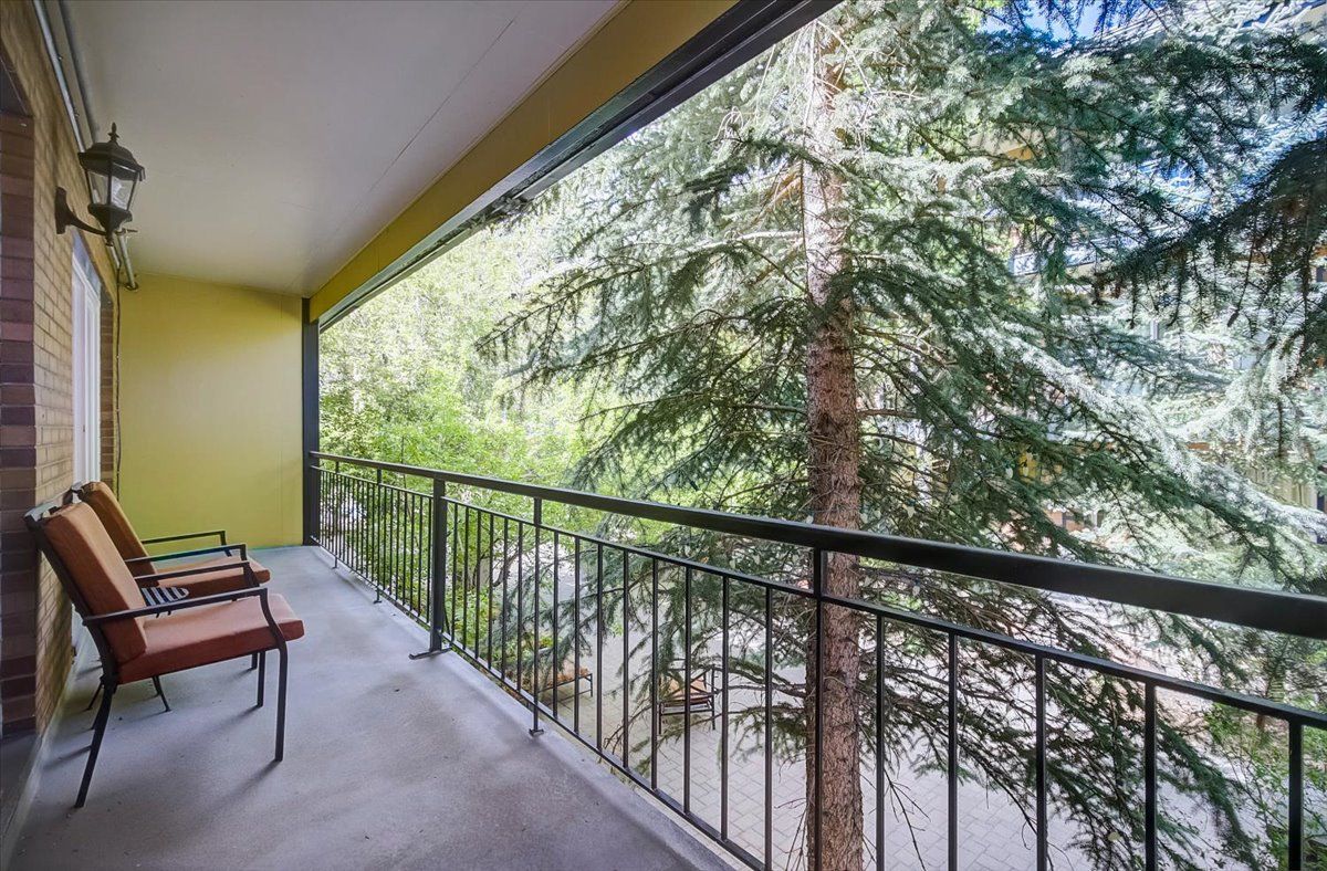 A balcony with a view of a coniferous forest, a bench, and a wall-mounted light fixture.