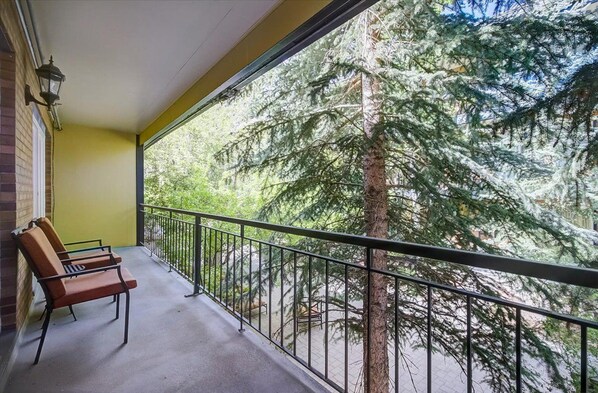 A balcony with a view of a coniferous forest, a bench, and a wall-mounted light fixture. - Treasure Mountain Inn - Main Street Condo - Top Floor (Park City)
