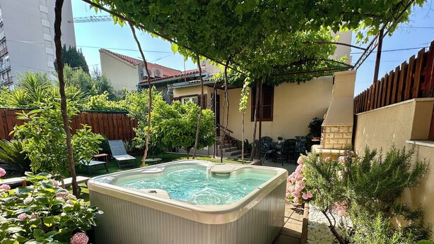 A hot tub surrounded by lush greenery and a patio area with outdoor furniture.