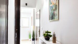 A hallway with a white console table, potted plants, and a framed artwork on the wall.