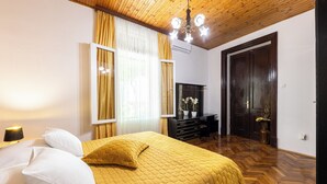 A hotel room with a wooden ceiling, a bed with white and yellow bedding, a desk with a mirror, and a door leading to another room.