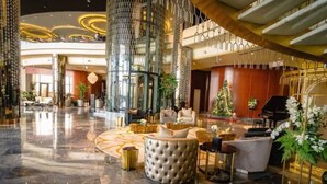 A spacious lobby with a marble floor, a central seating area with sofas and a round ottoman, and a Christmas tree. - Luxury 2BR Apartment in Paramount Towers Business Bay (Dubai)