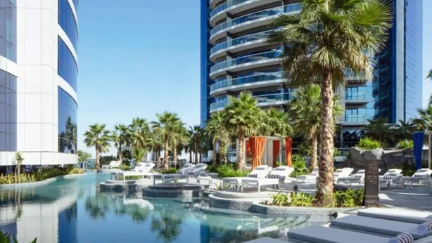 A modern hotel with a pool area, lounge chairs, and palm trees. - Luxury 2BR Apartment in Paramount Towers Business Bay (Dubai)