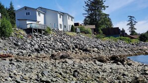 A coastal house with a rocky shoreline, a small deck, and a view of the sea. - {Forget-Me-Not Inn} Alaskan Waterfront Vacation Rental (Deer Suite) (Sitka)