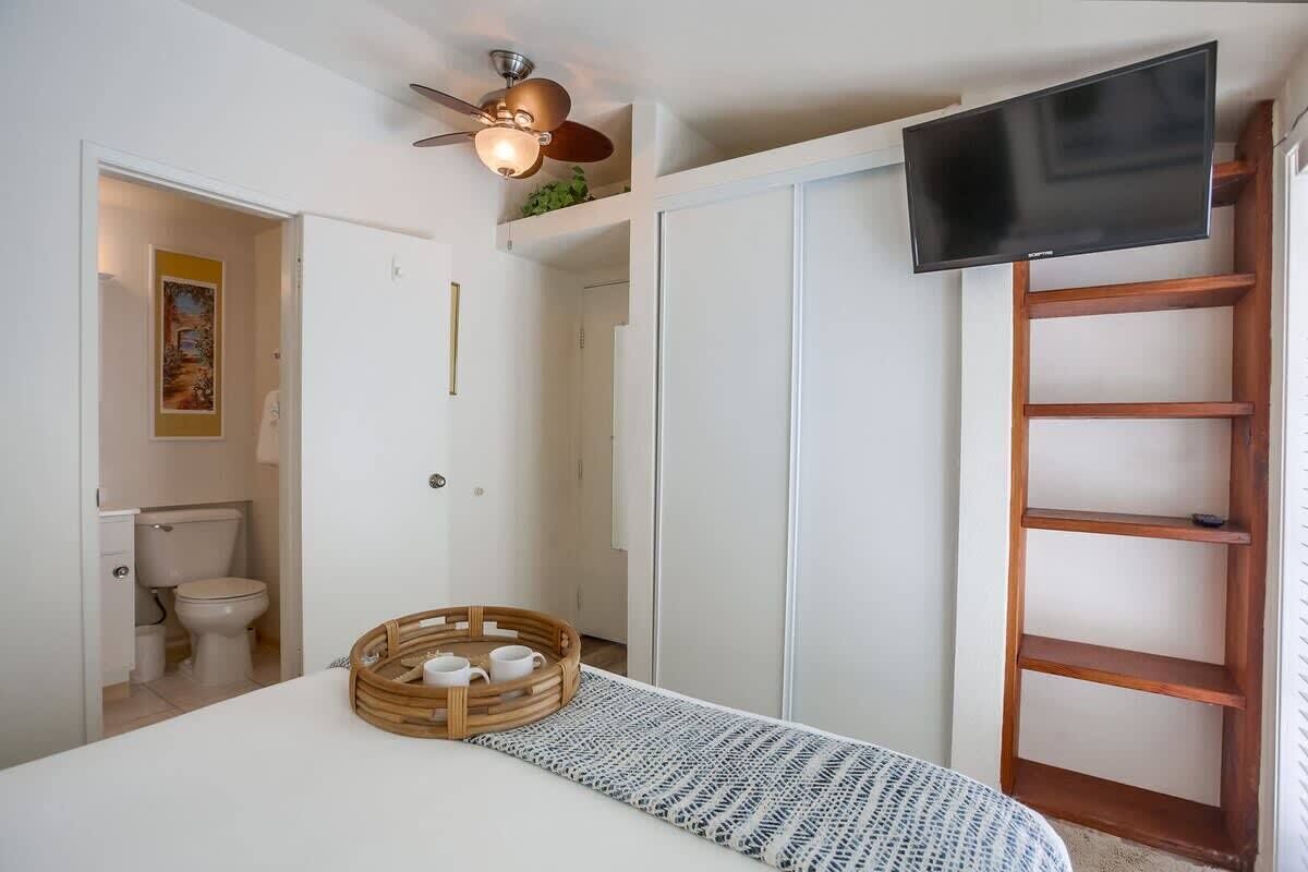 Une chambre à coucher comprenant un lit, un téléviseur, un ventilateur de plafond, une échelle en bois et une porte donnant sur une salle de bain.
