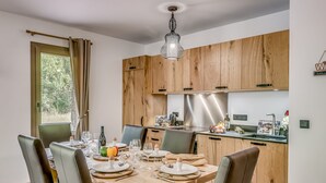 A modern kitchen with wooden cabinets, a stainless steel range hood, and a dining area set for four with a wooden table and chairs.
