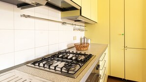 A kitchen with a gas stove, white tiles, yellow cabinets, and a stainless steel range hood. - APPARTAMENTI SECCHETO - BELLAVISTA (Campo nell'Elba)