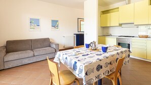 A cozy living area with a sofa and a dining table set for two, a kitchen with yellow cabinets, and a radiator. - APPARTAMENTI SECCHETO - BELLAVISTA (Campo nell'Elba)
