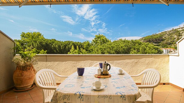 A terrace with a table set for two, a potted plant, and a view of a hillside. - APPARTAMENTI SECCHETO - BELLAVISTA (Campo nell'Elba)