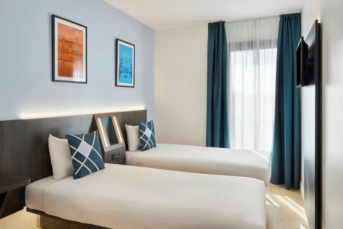 A hotel room with two beds, a flat-screen TV, and two framed pictures on the wall.