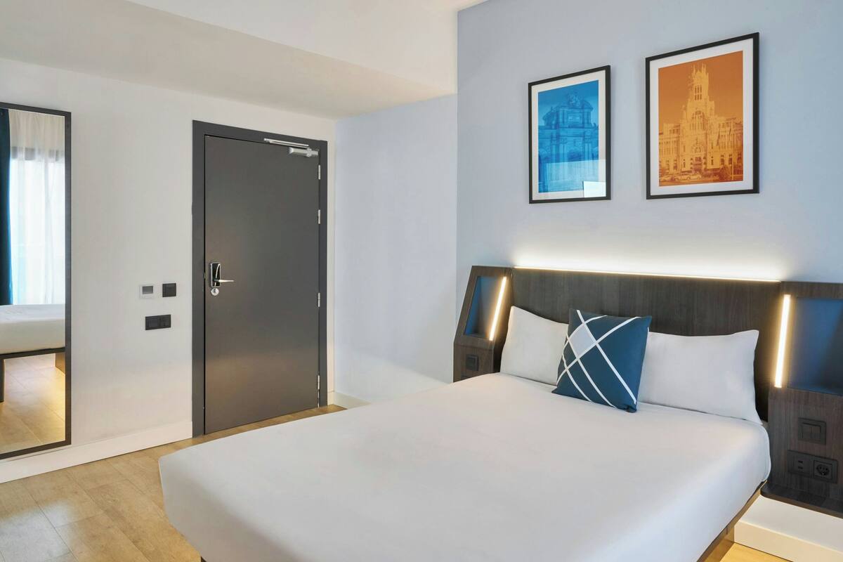 A hotel room with a bed, a door, and two framed pictures on the wall.