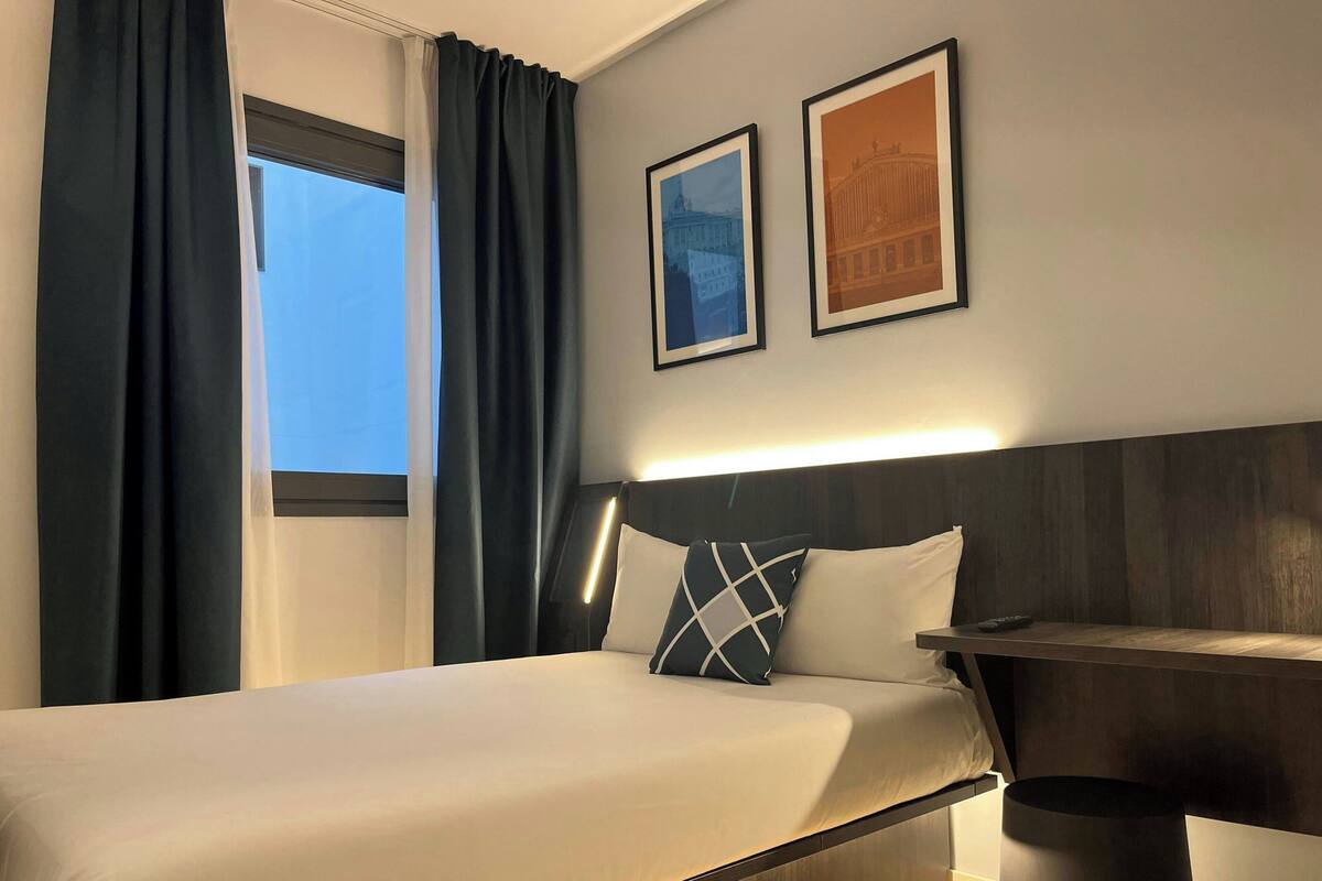 A hotel room with a bed, a nightstand, and two framed pictures on the wall.