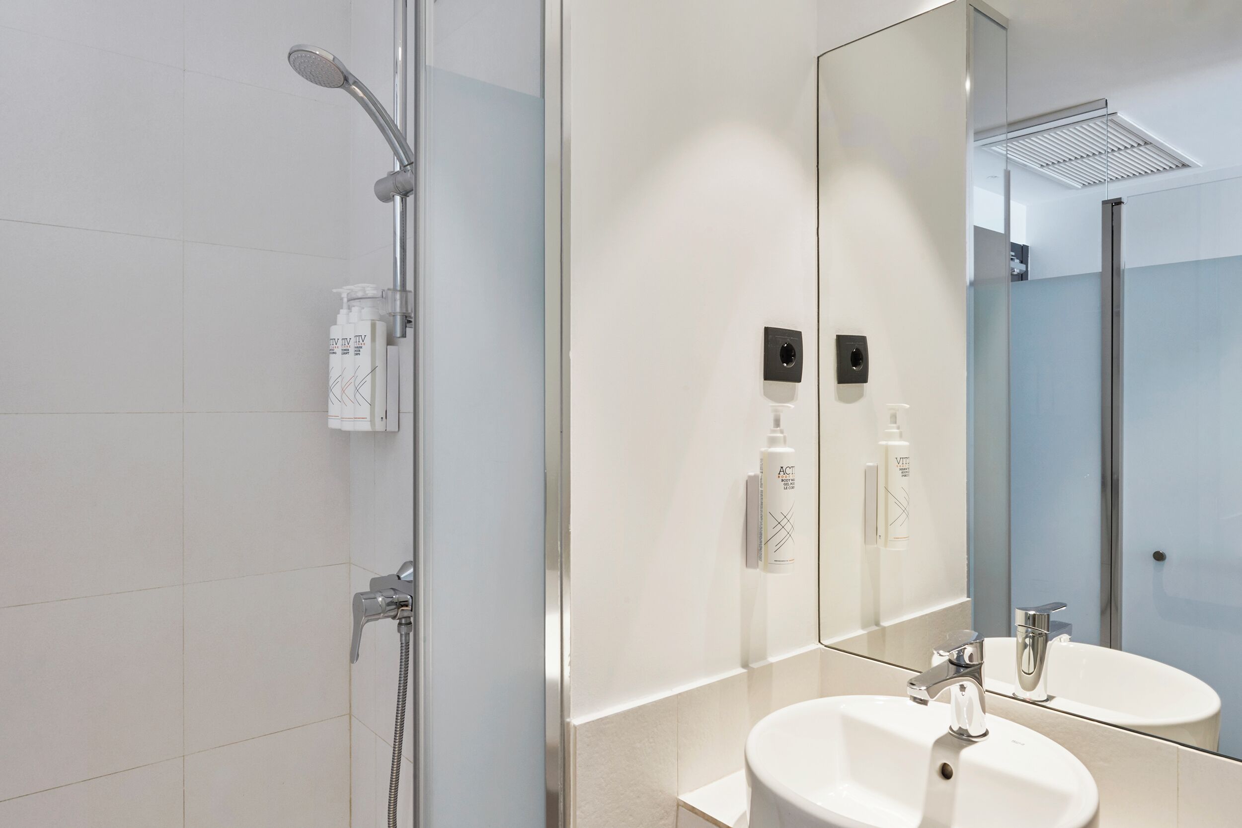 A modern bathroom with a glass shower enclosure, a large mirror, and two sinks.