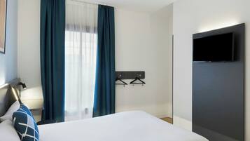 Een hotelkamer met een bed, een aan de muur bevestigde televisie en een raam met gordijnen.