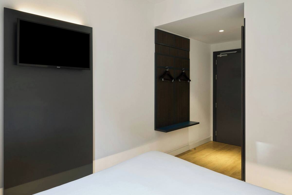 A modern room with a bed, a mounted TV, a wardrobe with a mirror, and a door.