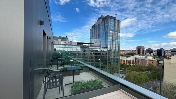 Un bâtiment moderne doté d’une façade en verre et d’une terrasse sur le toit avec des espaces de détente en plein air.