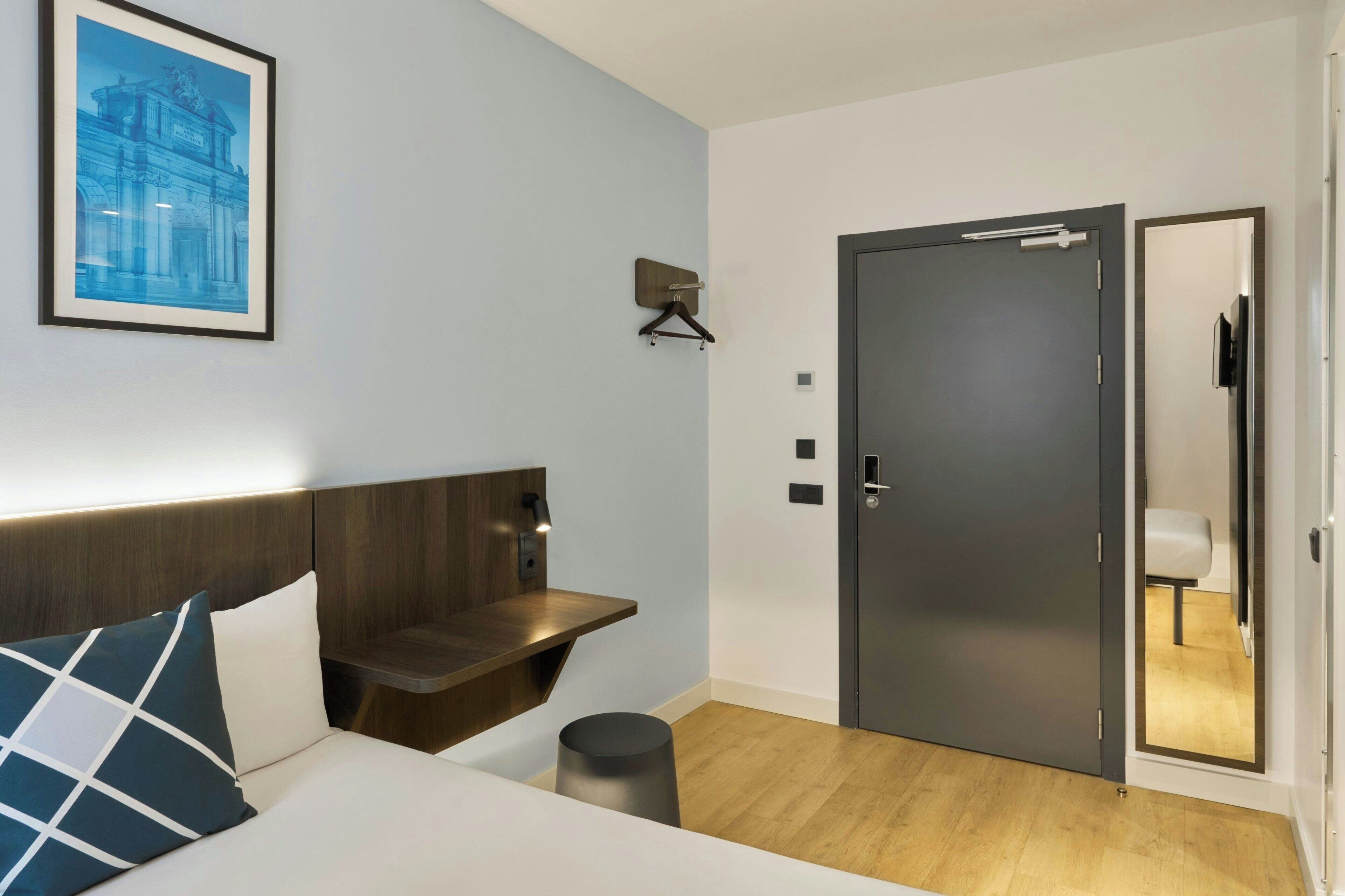 Una habitación de hotel moderna con cama, mesita de noche y una puerta con espejo.
