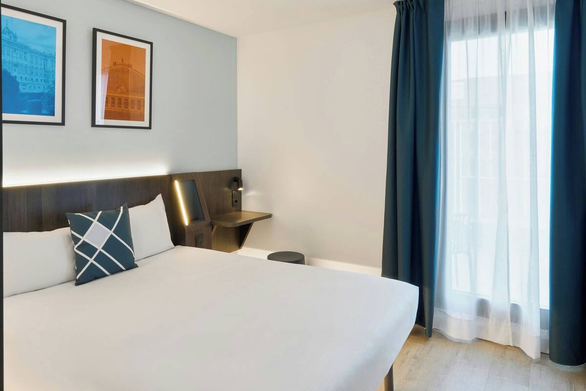 A hotel room with a bed, a nightstand, a lamp, and two framed pictures on the wall.