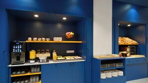 Un espace cuisine aux tons bleutés, comprenant une machine à café, des étagères remplies de produits alimentaires et un panier de fruits.
