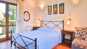 A bedroom with a bed, bedside tables, a chair, a window, and wall-mounted artwork. - Perone, two-room apartment in a villa in Marina di Campo, with equipped garden, covered parking spac (Campo nell'Elba)