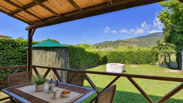 An outdoor patio with a table, chairs, and a view of a grassy area with a wooden fence and a hill in the background. - Perone, two-room apartment in a villa in Marina di Campo, with equipped garden, covered parking spac (Campo nell'Elba)
