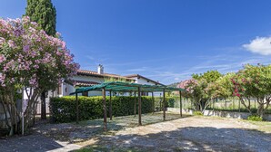 A covered outdoor area with a pergola, surrounded by flowering trees and a house with a tiled roof. - Perone, two-room apartment in a villa in Marina di Campo, with equipped garden, covered parking spac (Campo nell'Elba)