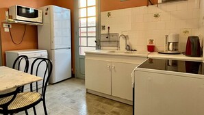 Een compacte keuken met een magnetron, koelkast en wastafel. Er is een eettafel met stoelen en een raam dat natuurlijk licht binnenlaat.