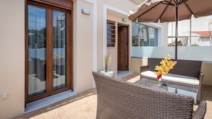 A balcony with wicker furniture, a glass table, and a potted plant. - Luxury Katsoulakis Apartments (Alikianos)