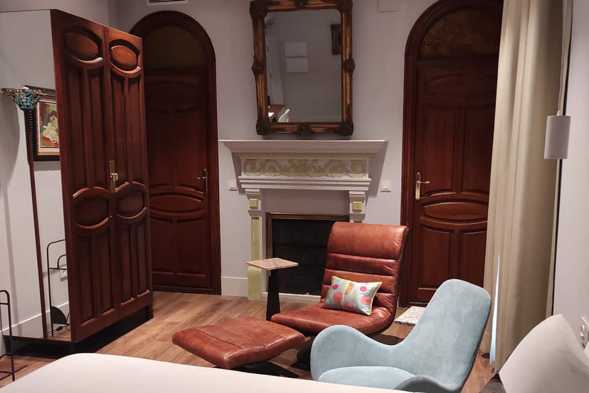 A bedroom with a bed, a chair, a sofa, a fireplace, and two doors.