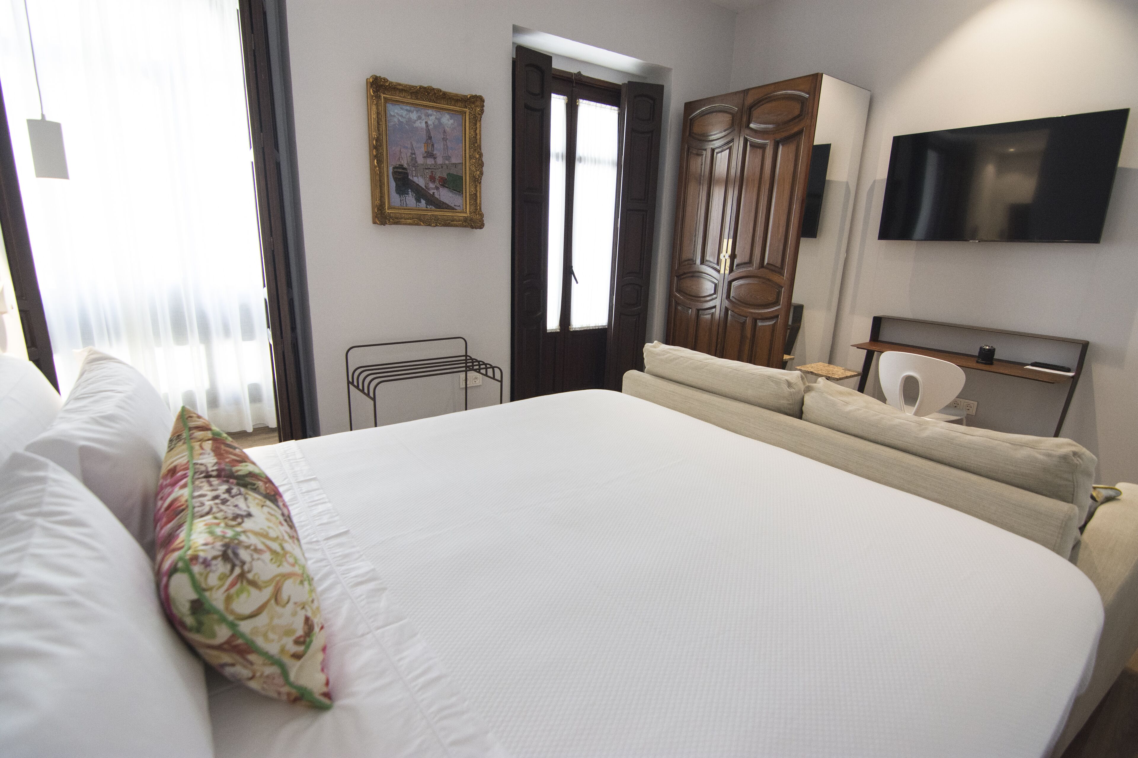 Habitación de hotel con una cama grande, un televisor montado en la pared y una puerta que da a otra habitación.