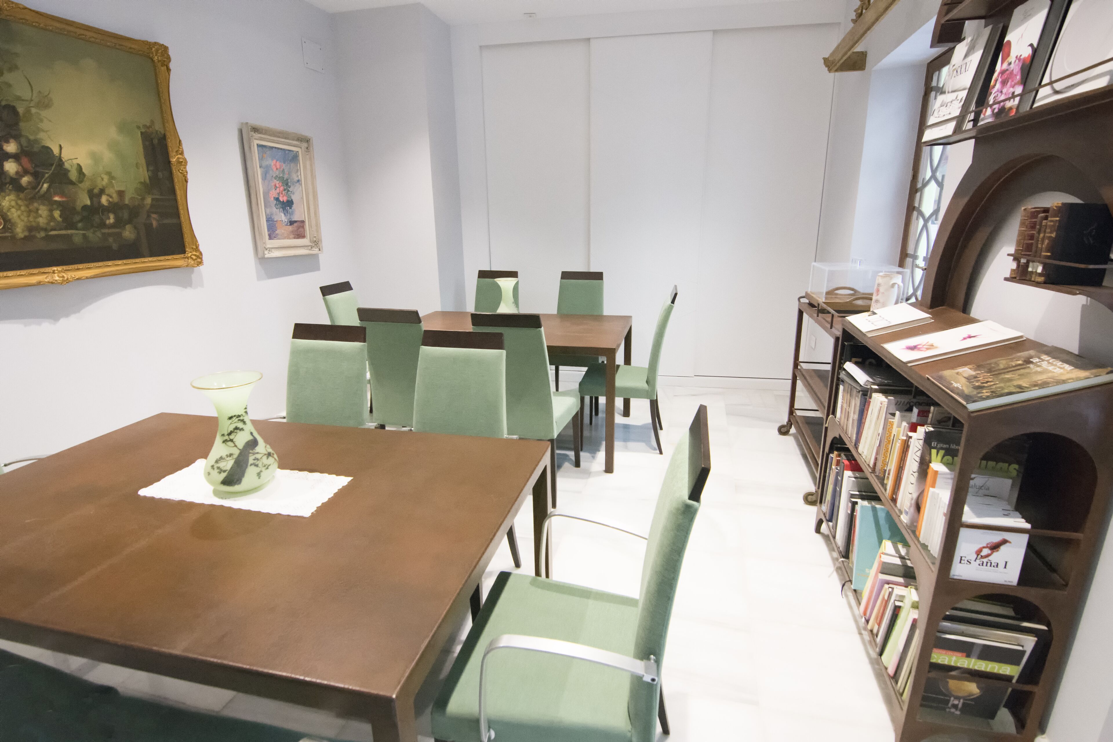 Un coin repas avec une table en bois et des chaises vertes, une bibliothèque remplie de livres et des œuvres d’art encadrées accrochées aux murs.