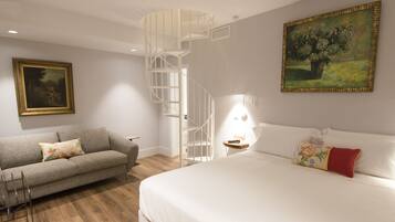 Un dormitorio moderno con una cama grande, un sofá gris, una escalera de caracol, un cuadro y una mesita de noche con una lámpara.