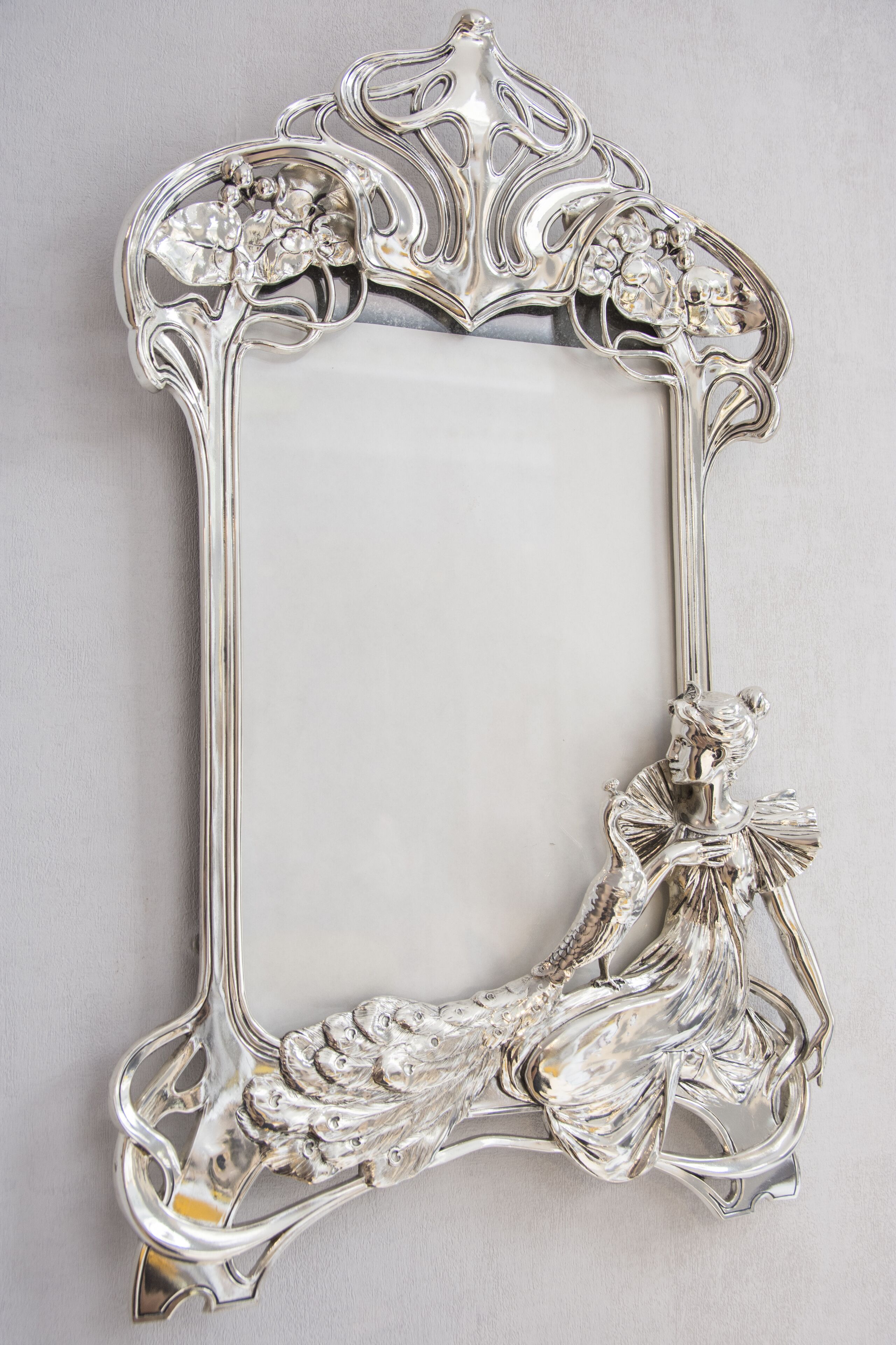 A silver ornate mirror with a floral design and a cherub figure.