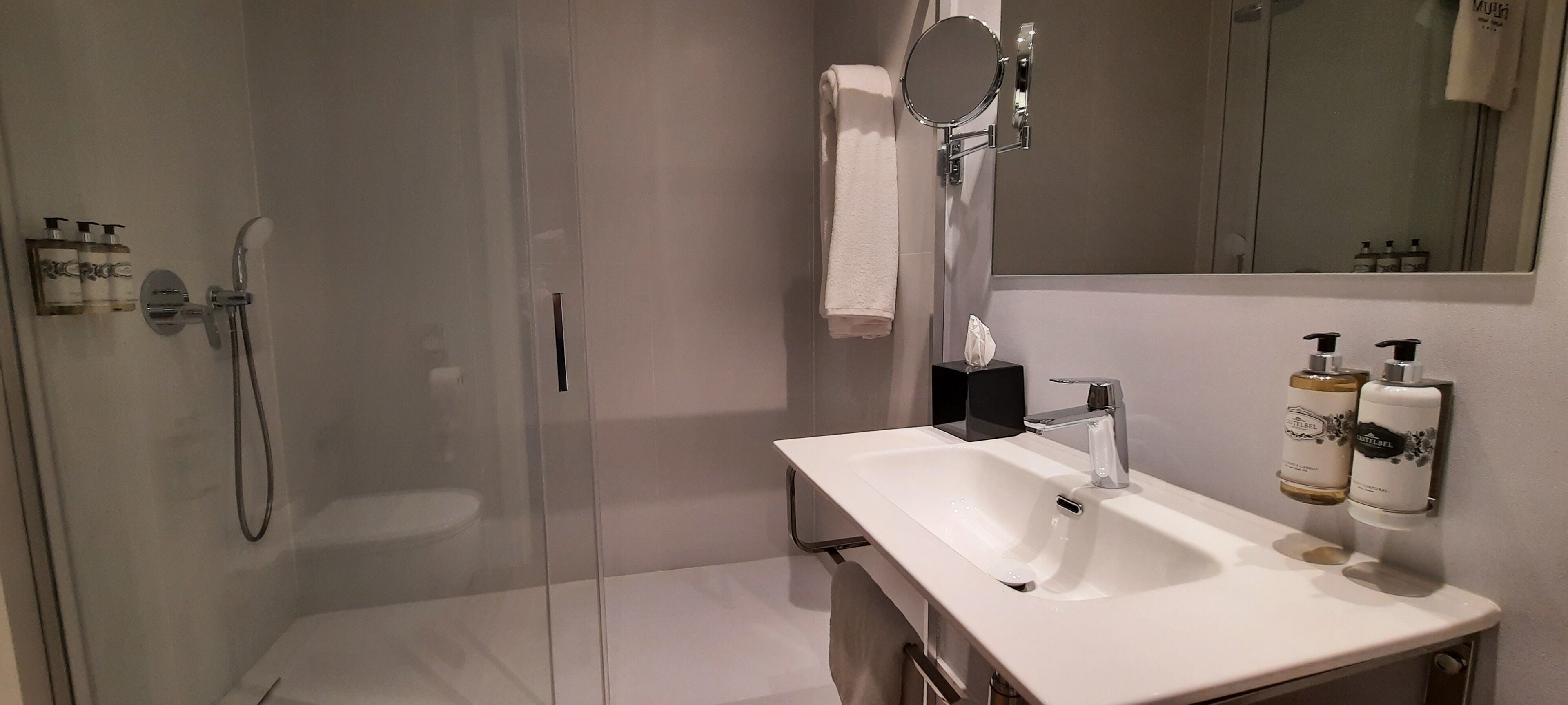 Um banheiro moderno com chuveiro em cabine de vidro, pia branca com espelho acima e amenities na parede.
