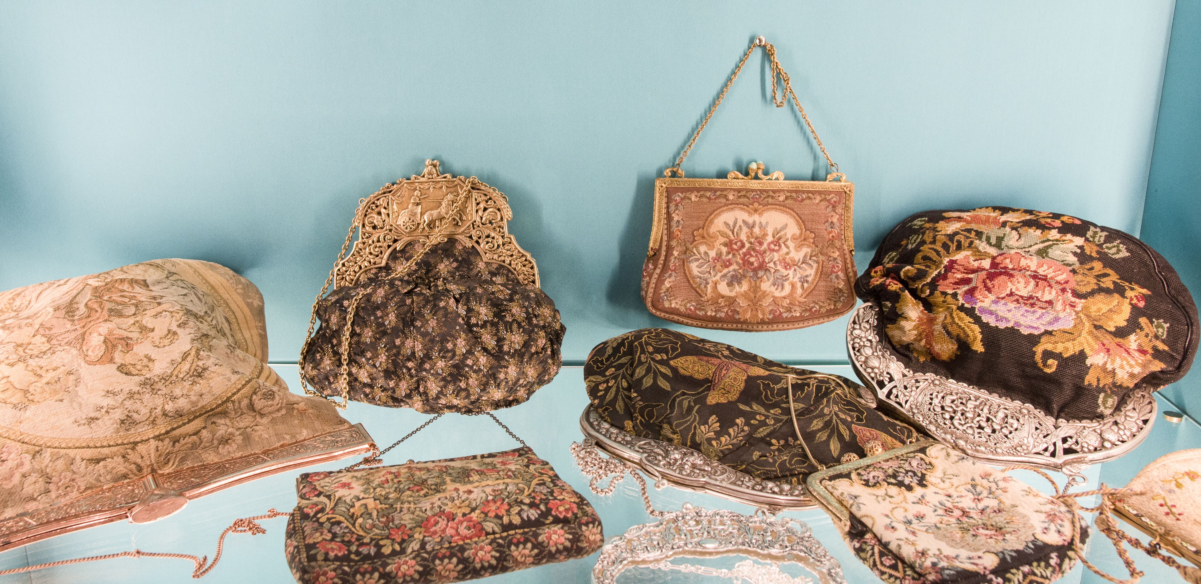A collection of vintage-style handbags and hats displayed against a light blue background.