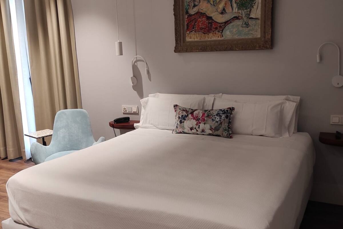 A large bed with white linens, a floral pillow, and a painting above it.