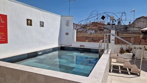 A rooftop pool with clear blue water, surrounded by a white wall with a red sign, and a staircase leading to the roof. - Hotel Oleum (Andujar)