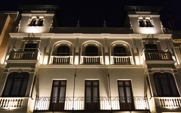 Un edificio con una fachada simétrica, varios balcones con barandillas de hierro forjado y ventanas regularmente espaciadas.