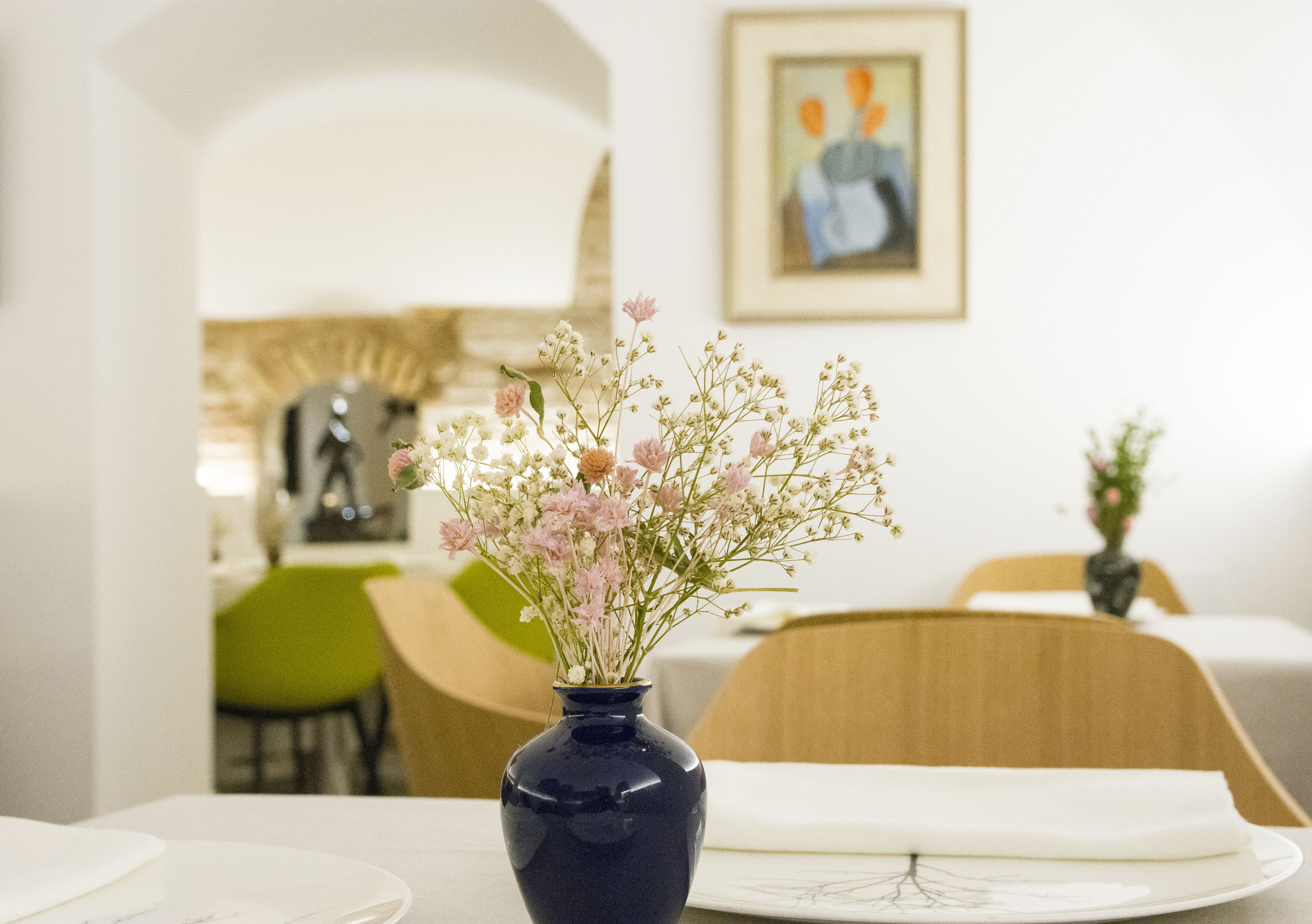 Una mesa de comedor con un jarrón de flores, una obra de arte enmarcada en la pared y una silla verde al fondo.