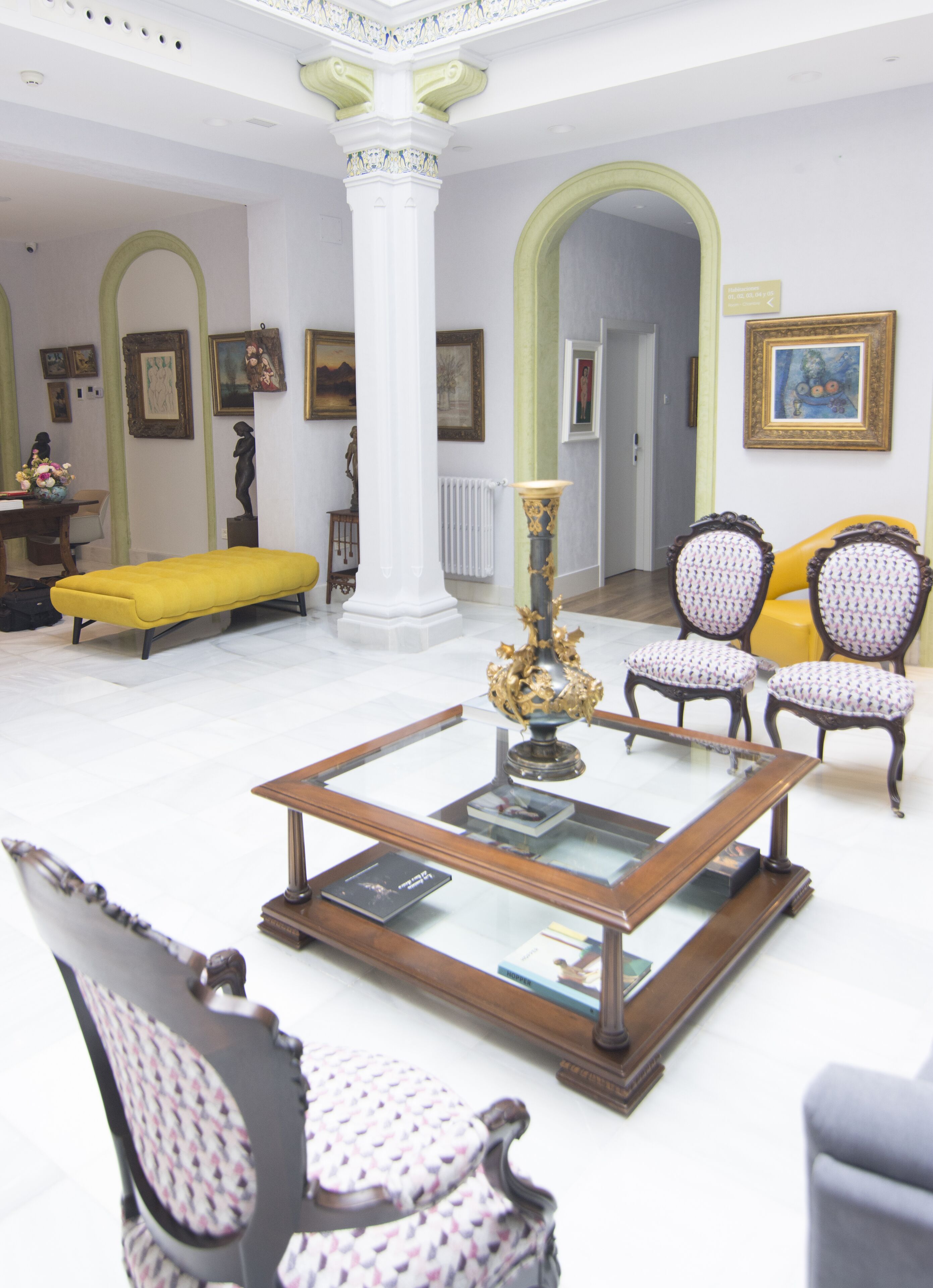 A spacious living room with a glass coffee table, a yellow sofa, and patterned chairs.