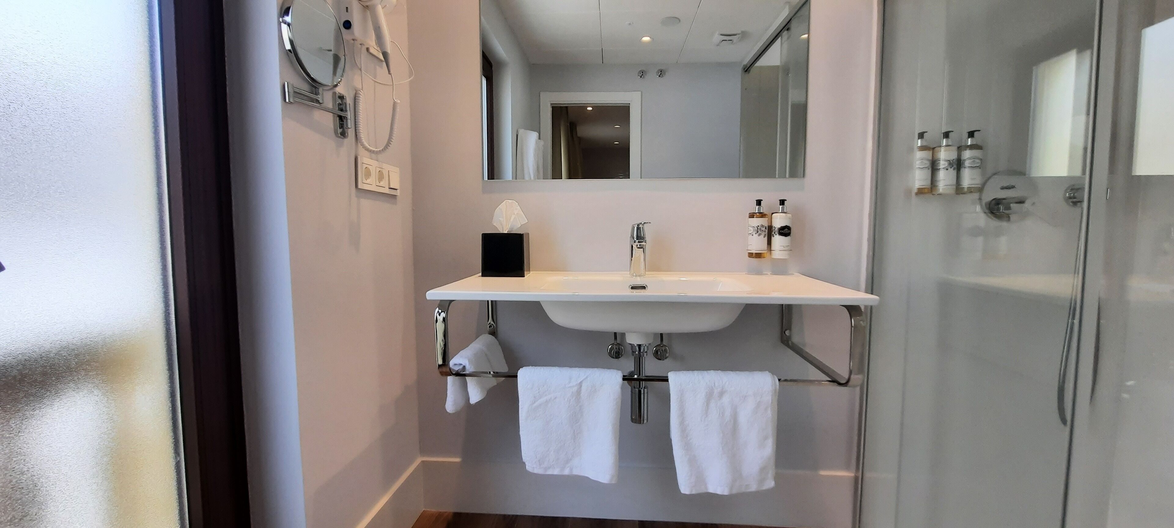 Un baño moderno con un lavamanos blanco, dos toalleros, una cabina de ducha de vidrio y un espejo sobre el lavamanos.