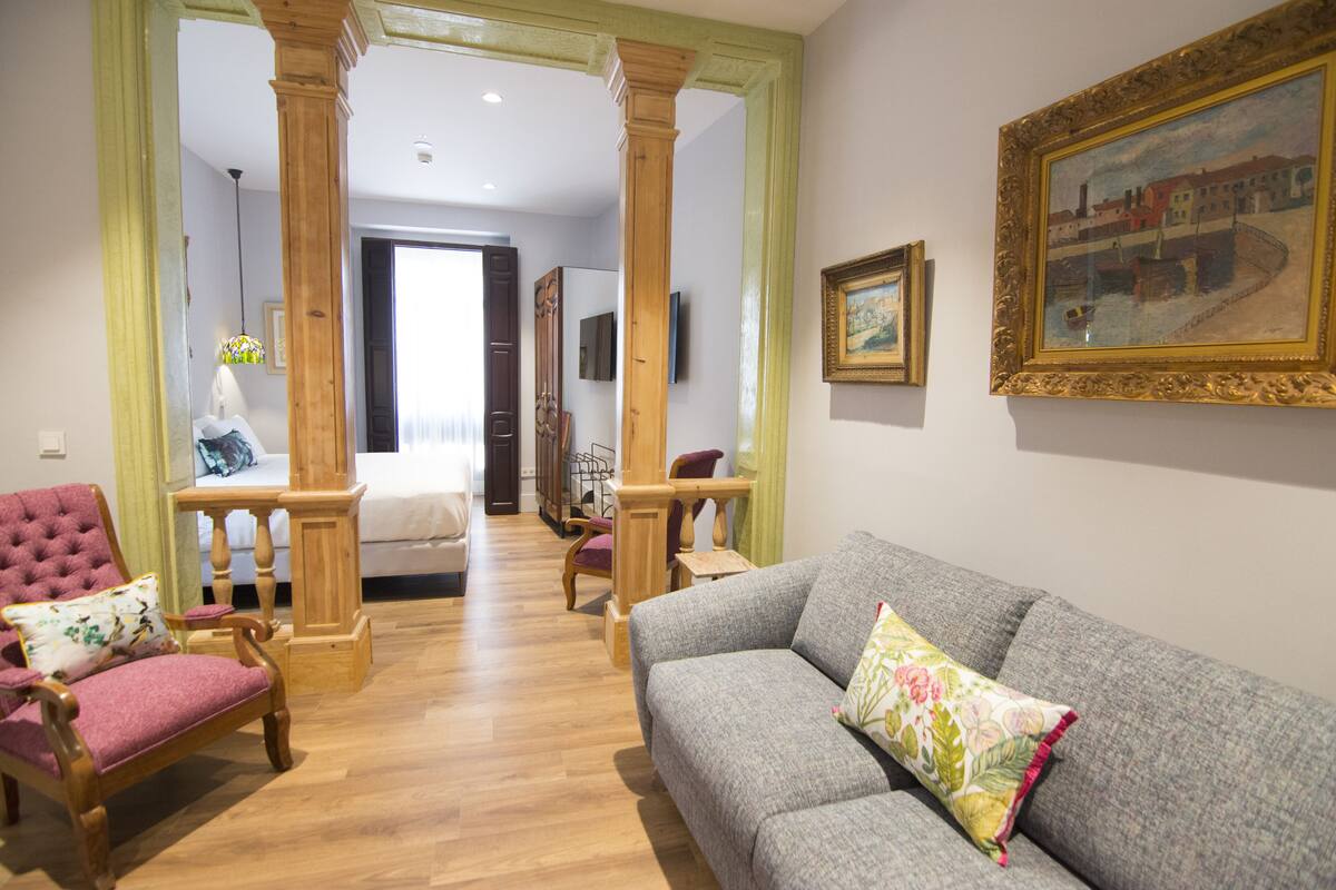 A living room with a grey sofa, a pink armchair, wooden furniture, and a painting on the wall.