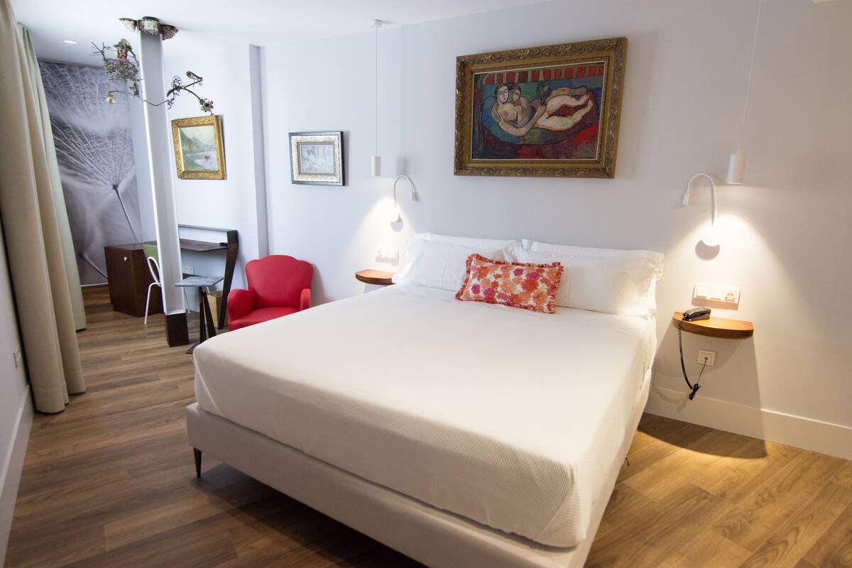 A hotel room with a large bed, a desk, a chair, and a painting on the wall.
