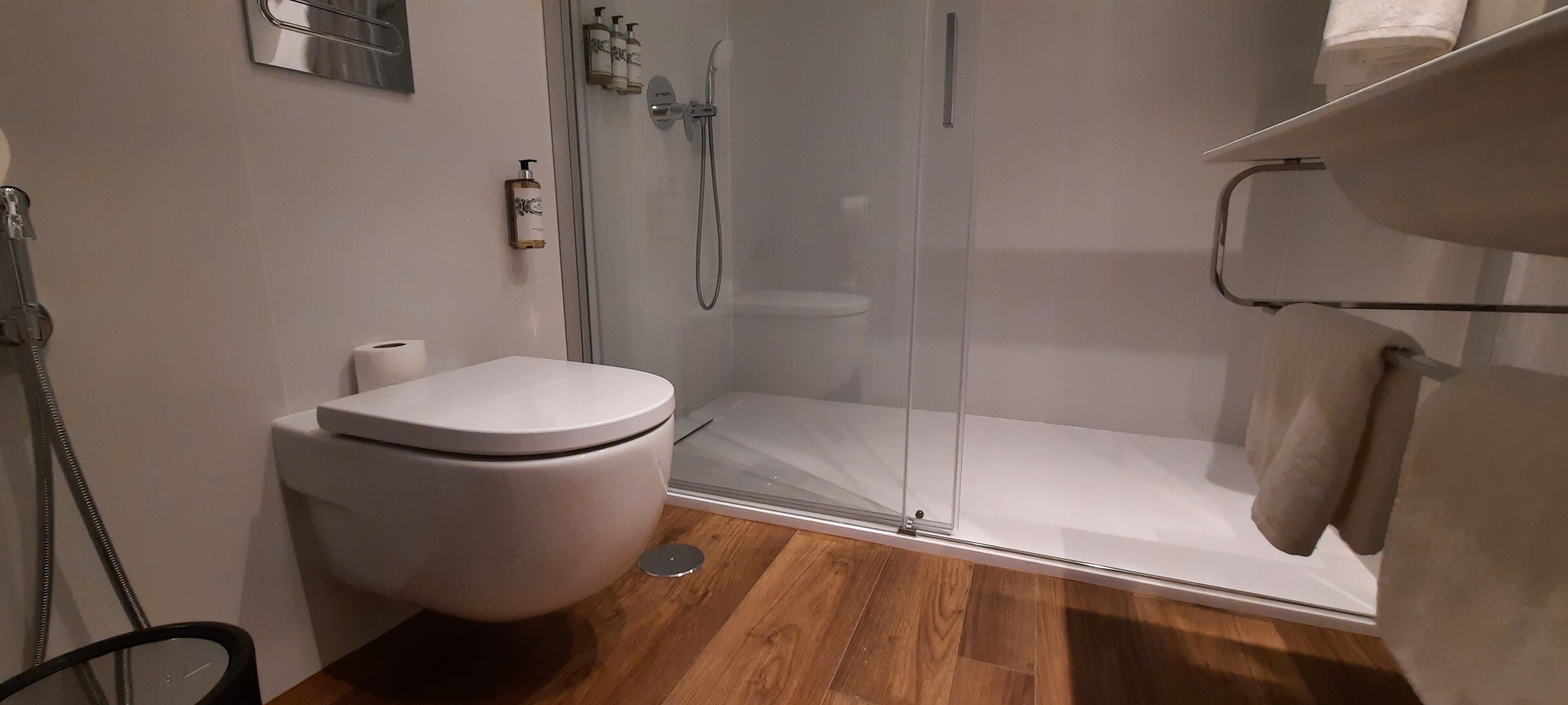 Un bagno moderno con il water, una cabina doccia in vetro e un pavimento in legno.