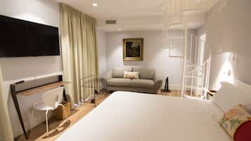 Habitación de hotel con cama, escritorio, silla, televisión, un cuadro y una escalera de caracol.