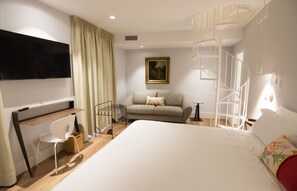 A hotel room with a bed, a desk, a chair, a TV, a painting, and a spiral staircase. - Hotel Oleum (Andujar)