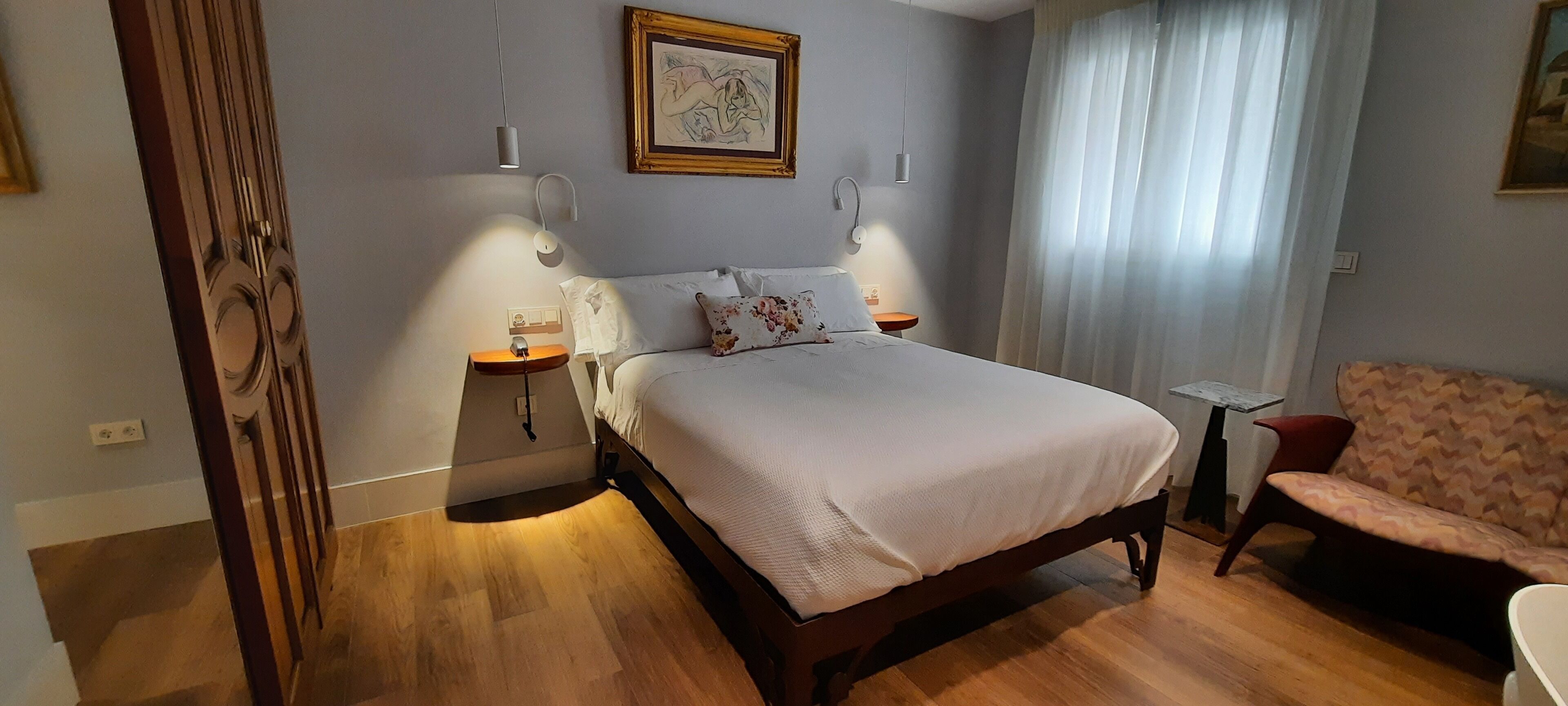 A bedroom with a wooden bed, bedside tables, a chair, and a painting on the wall.