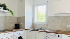 A compact kitchen with a washing machine, a dishwasher, a window, and a plant on the countertop.